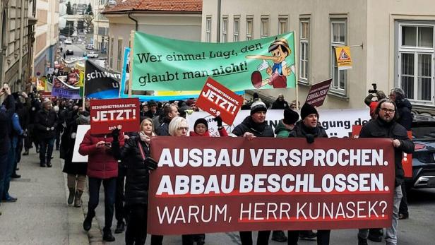 Demonstrierende Menschen mit Transparenten und Schildern ziehen durch eine enge Straße in einer Stadt.