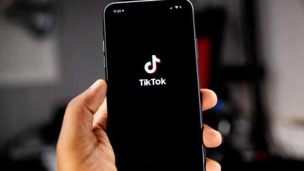 Hand hält Smartphone mit geöffnetem TikTok-Startbildschirm.
