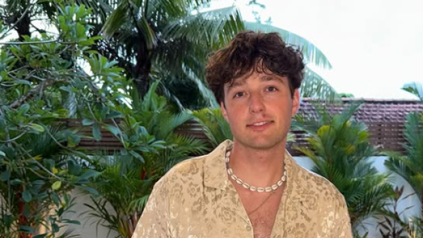 Tucke Genal steht in einem gold schimmernden Hemd vor einem Pool.