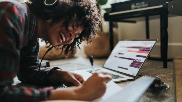 Frau hört lachend Musik vor einem Laptop
