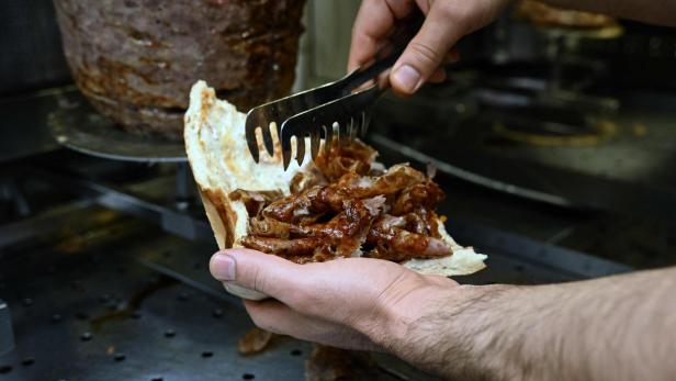 Ein Döner wird mit einer Zange mit Fleisch gefüllt.