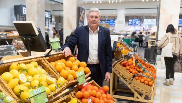 Ein Mann im Anzug steht an einer Obsttheke mit Zitronen, Orangen und anderen Zitrusfrüchten in einem Supermarkt.