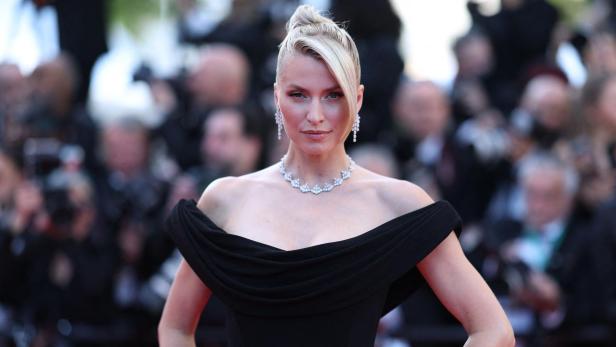 Lena Gercke mit hochgesteckten Haaren trägt ein schwarzes Kleid und Schmuck vor einem verschwommenen Hintergrund.