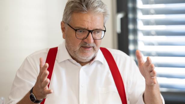 Peter Hacker gestikuliert wild. Er trägt ein weißes Hemd und rote Hosenträger.