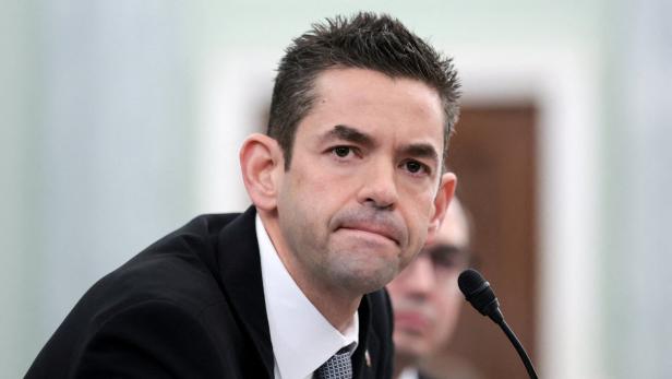 Ein Mann im Anzug spricht ernsthaft in ein Mikrofon bei einer formellen Veranstaltung.