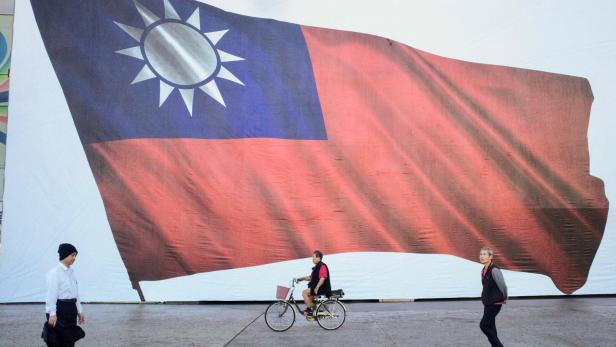 Eine Person fährt Fahrrad vor einer großen Flagge von Taiwan, während andere zu Fuß unterwegs sind.