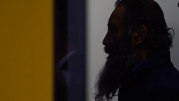 Ein Mann mit Bart und dunklen Haaren ist im Profil vor einem gelben Hintergrund zu sehen.