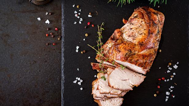 Roasted sliced Christmas ham of turkey on dark rustic background. Top view. Festival food.