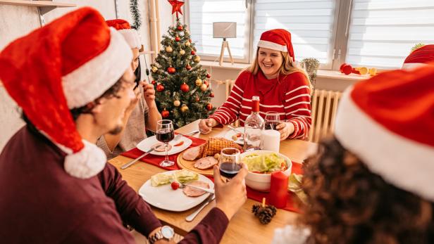 Menschen sitzen zusammen beim Tisch bei einem Weihnachtsessen.