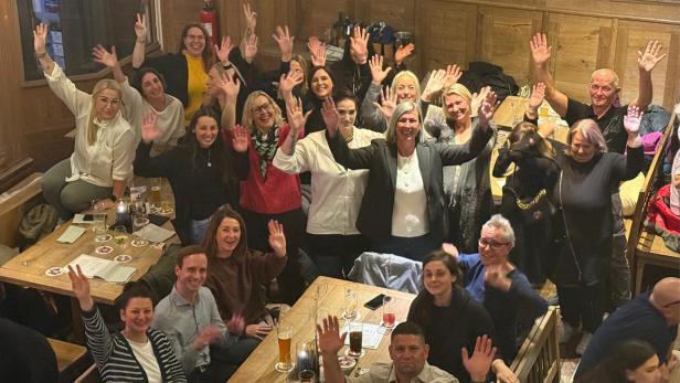Gruppe von Menschen sitzt und steht in fröhlicher Stimmung in einem Restaurant und winkt.