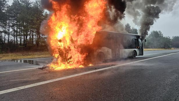 Eine Aufnahme von einem Autobus, der mitten auf einer Straße vollkommen in Flammen steht.