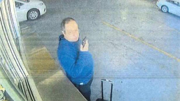 Ein Mann mit blauem Pullover steht in einer Tiefgarage neben einem Rollkoffer und hält ein Handy ans Ohr.