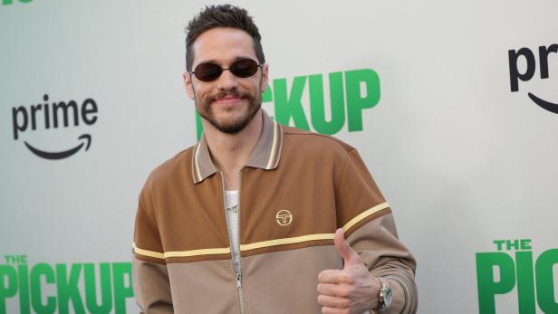 Pete Davidson mit Sonnenbrille und brauner Jacke zeigt den Daumen nach oben.