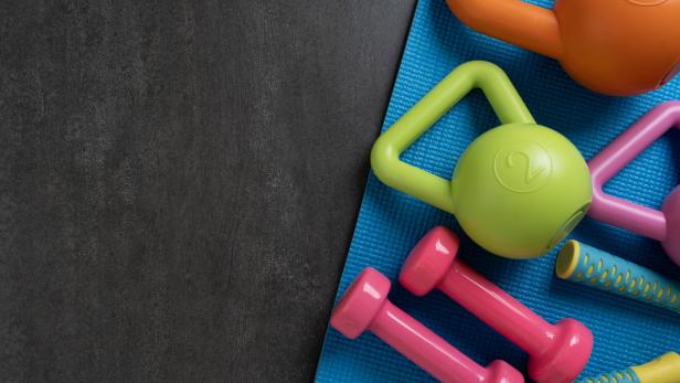 Auf einer blauen Matte liegen bunte Hanteln und Kettlebells neben einer dunklen Fläche.