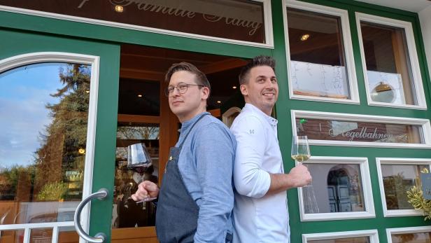 Markus und Thomas Haag mit einem Weinglas in der Hand vor ihrem Wirtshaus.  