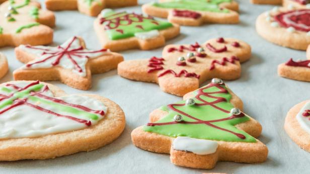 Verschieden geformte Weihnachtskekse mit bunter Zuckerglasur und Dekor liegen auf Backpapier.