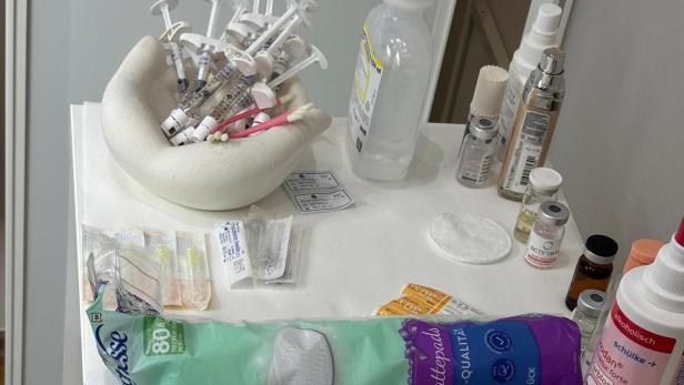 Mehrere Spritzen, Ampullen, Desinfektionsmittel, Wattepads und medizinische Utensilien liegen auf einer weißen Ablage.