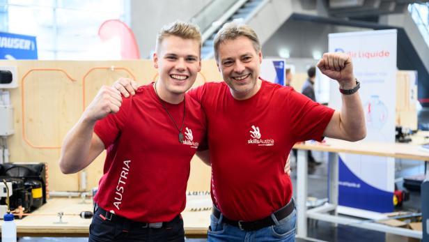 Zwei Männer in roten T-Shirts mit „skillsAustria“-Logo stehen lachend nebeneinander und zeigen eine Siegerpose.: Vater-Sohn-Team:  Jonas Danninger  (li.)  trainiert für  die Skills  mit seinem Vater  Rupert Danninger.
