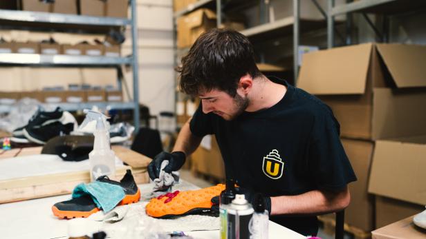 Ein Mann putzt ein Paar Schuhe mit unterschiedlichen Mitteln in einer Werkstatt