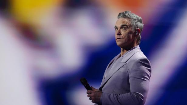 Robbie Williams im blasslila Anzug mit Mikro auf der Bühne