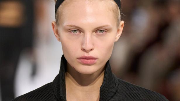 Eine sehr dezent geschminkte Frau im schwarzen Blazer mit schwarzem Haarband