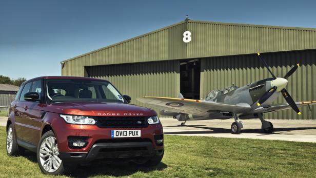 Ein roter Range Rover steht vor einem Hangar mit einem Spitfire-Flugzeug.