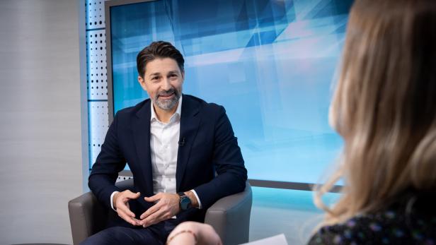 Ein Mann im Anzug sitzt in einem modernen Studio und spricht mit einer Frau, die ihm Fragen stellt.