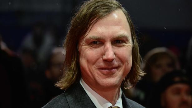 Ein Mann mit mittellangem braunem Haar trägt Anzug und Krawatte und lächelt in einer Menschenmenge.