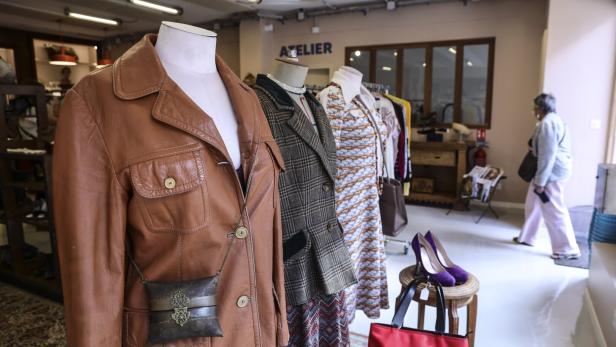 Drei Schaufensterpuppen mit Vintage-Kleidung und Accessoires stehen in einem hellen Laden, im Hintergrund läuft eine Frau vorbei.