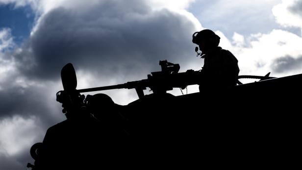 Silhouette eines Soldaten mit Waffe vor bewölktem Himmel.
