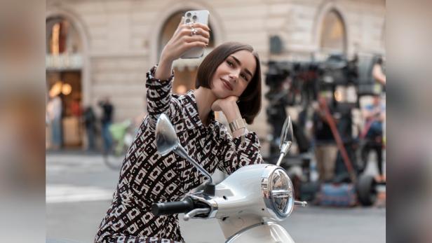 Lily Collins schießt als Emily ein Selfie auf einen Motorroller gestützt