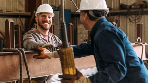 Zwei Männer mit Schutzhelmen unterhalten sich lächelnd.