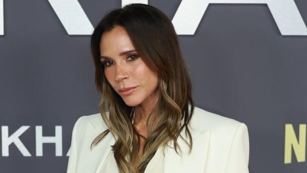 Eine Frau mit langen, braunen Haaren trägt ein elegantes, cremefarbenes Kostüm mit Bluse und Rock.