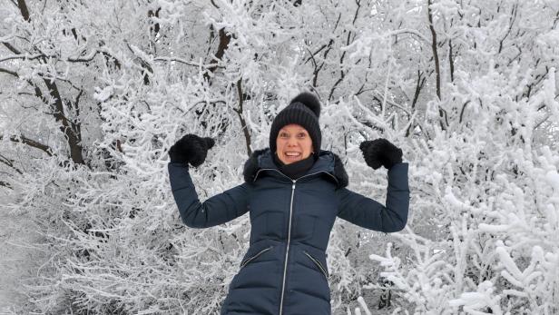 Eine Frau in einem Wintermantel im Schnee, die ihre Muskeln zeigt 