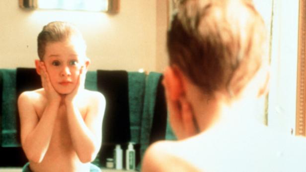 Ein Junge steht mit erschrockenem Gesichtsausdruck und Händen an den Wangen vor einem Badezimmerspiegel.