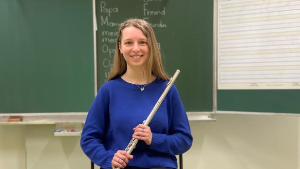 Kathrin Holzer sitzt vor einer Schultafel mit einer Querflöte in der Hand.