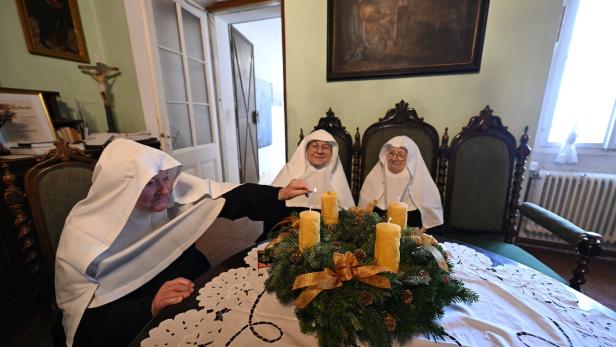 Drei Nonnen sitzen an einem Tisch mit Adventskranz und zünden Kerzen an.