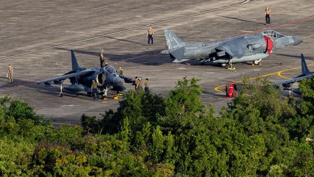 Zwei Militärflugzeuge stehen auf einem Flugfeld, umgeben von mehreren Personen und Bäumen im Vordergrund.