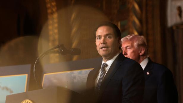 Marco Rubio spricht am Rednerpult, während Donald Trump im Hintergrund steht.