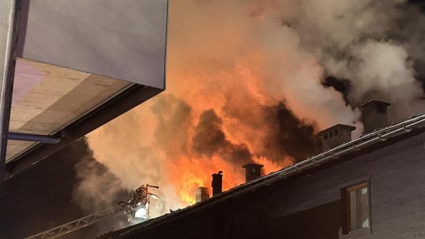 Flammen und dichter Rauch steigen aus dem Dachstuhl eines Gebäudes in der Nacht auf.