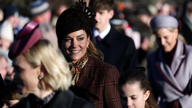 Kate Middleton mit Hut und kariertem Blazer lächelt inmitten einer Menschenmenge.