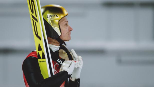 Ein Skispringer mit goldenem Uvex-Helm hält gelbe Fischer-Ski und trägt ZIENER-Handschuhe.