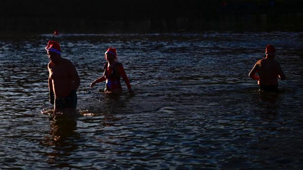 Drei Personen mit Weihnachtsmützen waten durch dunkles Wasser.
