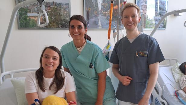 Katrin Teufel mit Besuchern in einem Bett im Krankenhaus.