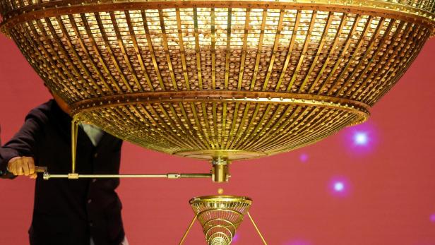 Eine goldene Lostrommel ist mit Kugeln gefüllt, während eine Kugel herausfällt.