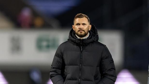 Ein Mann mit Bart und dunkler Jacke blickt ernst in die Kamera.