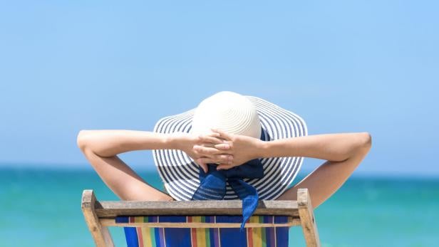 Eine Frau mit Hut entspannt im Liegestuhl am Strand.