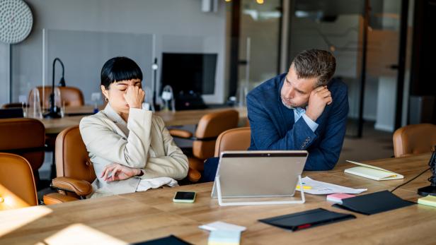 Zwei Geschäftsleute an einem Schreibtisch mit besorgten Mienen.