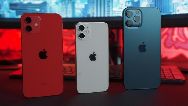 Drei iPhones in Rot, Weiß und Blau stehen nebeneinander vor einer Tastatur und Monitor.