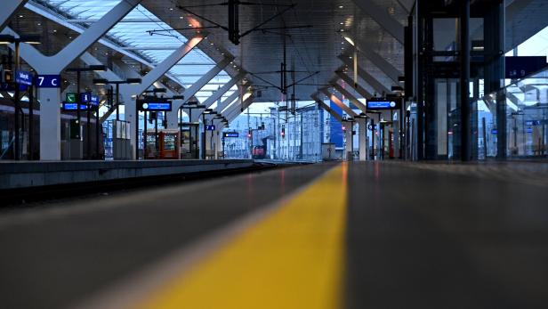 Ein leerer Bahnsteig mit gelber Sicherheitslinie und Anzeigetafeln unter einem modernen Dach.